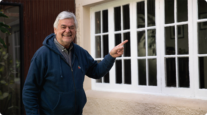 un hombre feliz indica con el dedo la ventana de madera que acaba de restaurar.