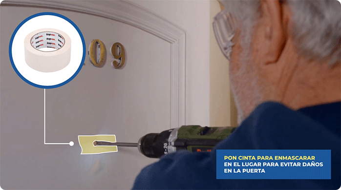 un hombre perfora una puerta para instalar una mirilla, usando una broca y cinta para enmascarar para proteger la superficie.