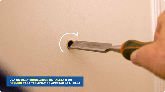un hombre aprieta la mirilla en la puerta usando un formón.