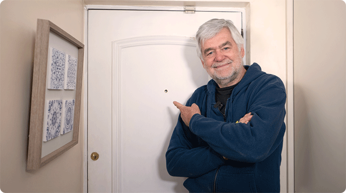 un hombre indica con el dedo la puerta en la que acaba de instalar una mirilla.