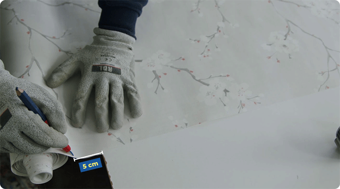 una persona con guantes de seguridad mide 5 cm de excedente en el papel mural para revestir las puertas del clóset.