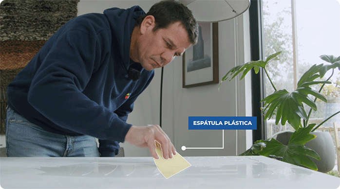 un hombre aplica adhesivo para papel mural en la puerta del clóset usando una espátula plástica.