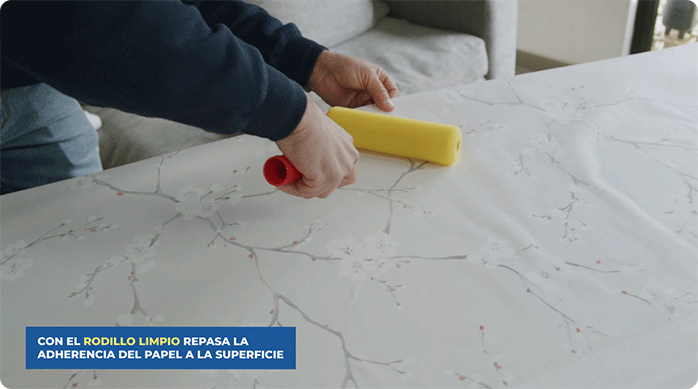 un hombre usa un rodillo espuma para alisar el papel mural recién pegado en una puerta de clóset.