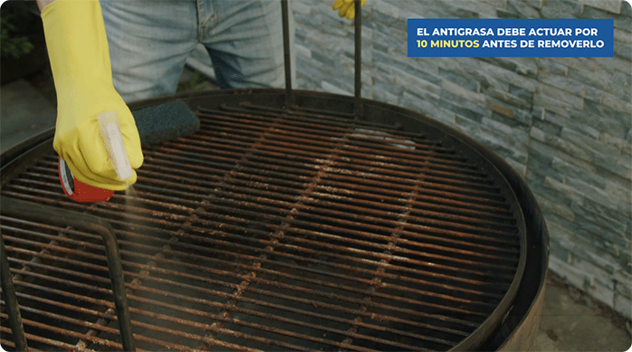 un hombre con guantes amarillos pulveriza antigrasa o desengrasante en una parrilla oxidada.
