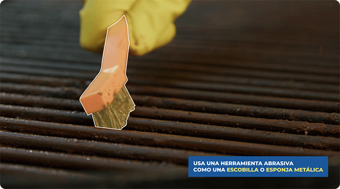 una persona pasa una escobilla metálica en la parrilla para eliminar el óxido superficial y la grasa.