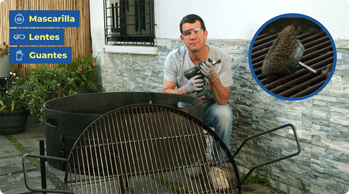 un hombre hincado al lado de una parrilla sosteniendo un taladro con una grata metálica en la punta.