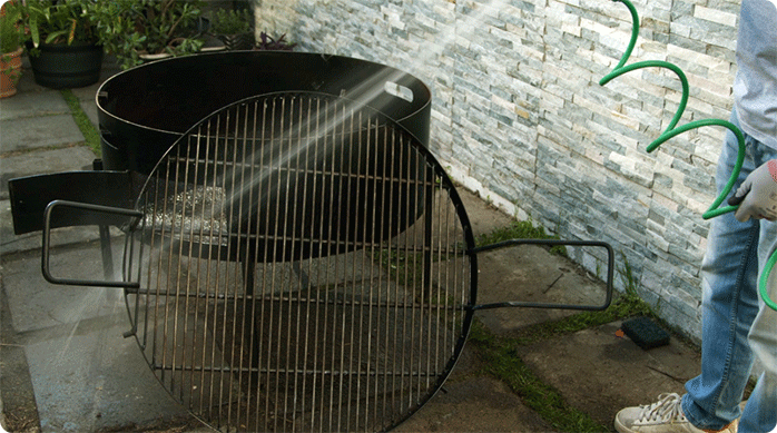 un hombre enjuaga una parrilla con una manguera.