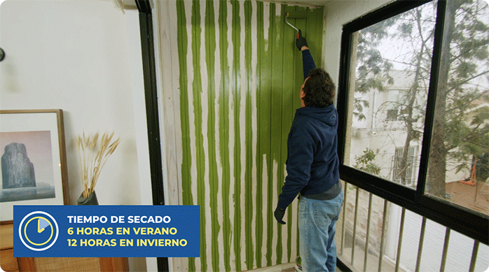 un hombre pinta un muro de madera en un balcón pequeño.