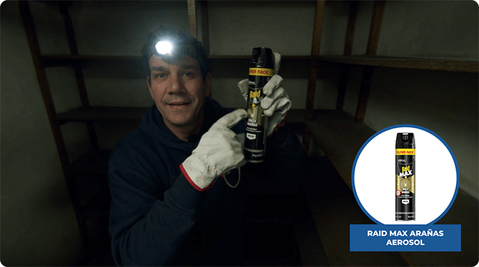 un hombre en una bodega oscura sostiene un aerosol raid max arañas