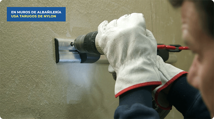 un hombre atornilla unos ganchos para colgar en el muro de la bodega de departamento.
