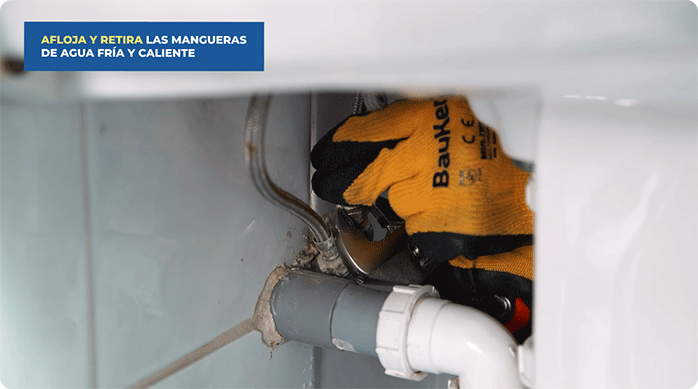 una persona con guantes de trabajo desenrosca los flexibles del agua del monomando.