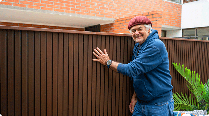 un hombre mayor muy feliz muestra cómo quedó el muro exterior con revestimiento wall panel 3D.