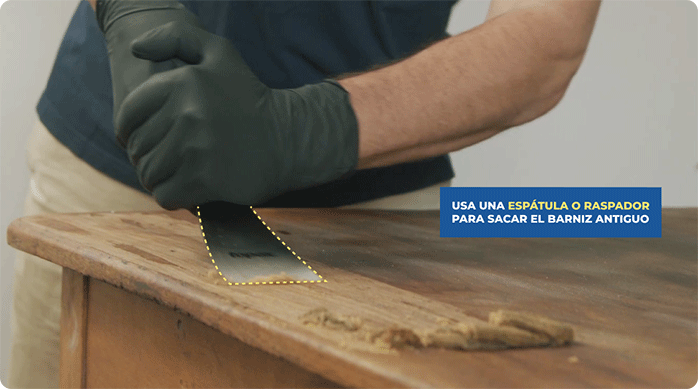 un hombre elimina el barniz de una mesa de madera usando una espátula.