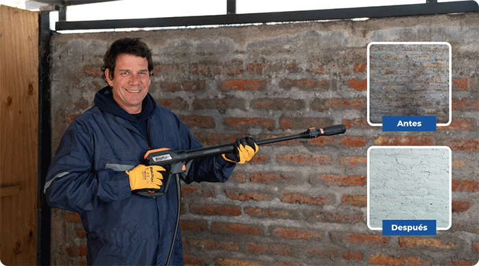 un hombre con overol y guantes sostiene en sus manos el mango de una hidrolavadora, frente a un muro exterior.