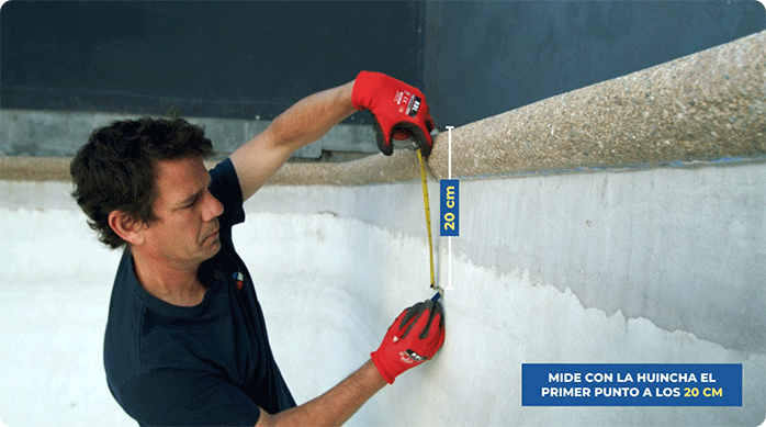 un hombre marca 20 cm desde el borde superior de la piscina hacia abajo, por su interior, para instalar las mallas mosaico.