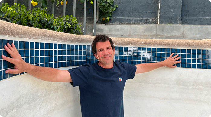 un hombre feliz dentro de una piscina vacía que acaba de decorar con mosaicos.