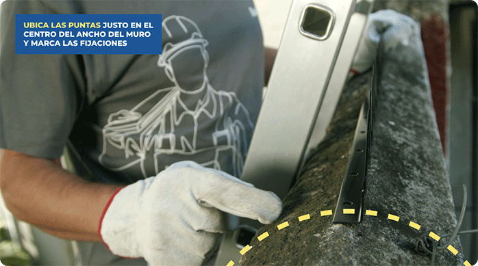 un hombre indica con el dedo el lugar donde instalará las puntas de protección en el muro: justo en el centro del ancho del muro.