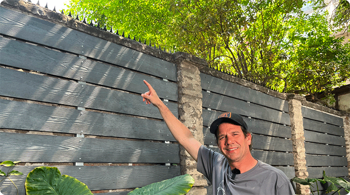 un hombre sonriendo indica con el dedo las puntas de protección que acaba de instalar en la parte superior de un muro exterior.