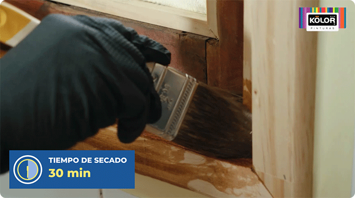una persona aplica stain lasur en el nuevo marco de madera de la ventana.