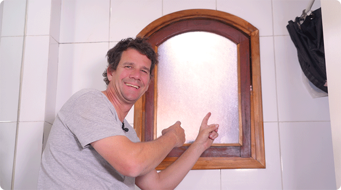 un hombre sonriendo indica la ventana a la que le renovó el marco de madera.