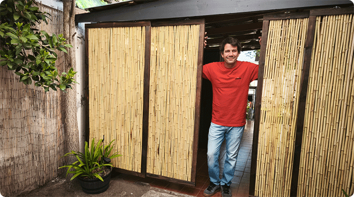 un hombre sonríe apoyado en su nuevo cierre de terraza con paneles de caña que acaba de instalar.