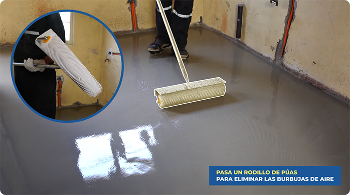 un hombre pasa un rodillo de púas en el piso con autonivelante weberfloor para eliminar burbujas de aire.