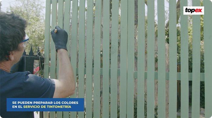 un hombre aplica pintura látex en un treillage de madera.