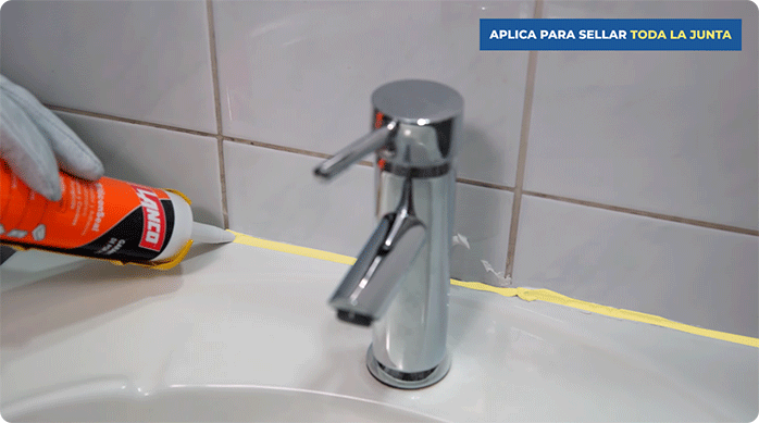 un hombre aplica sellador para baño y cocina lanco en la juntura de un lavamanos con el muro.