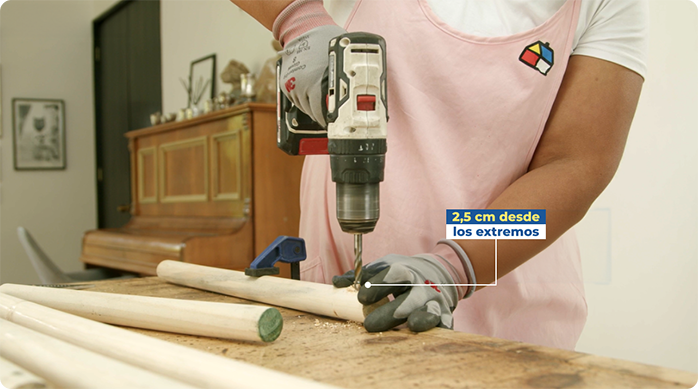 una mujer hace perforaciones en un tarugo de madera con un taladro.