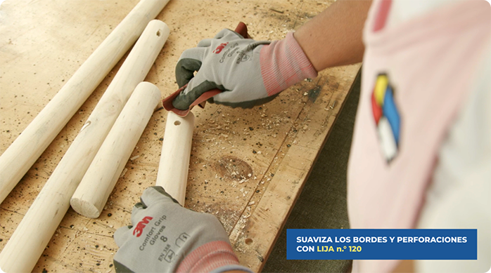 una mujer suaviza las perforaciones y cortes que hizo en un tarugo de madera usando una lija n.° 120.