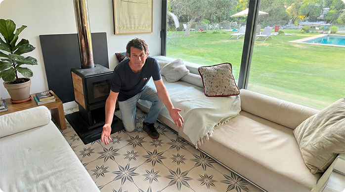 un hombre hincado muestra muy feliz un piso de cerámica con su fragüe recién reparado.