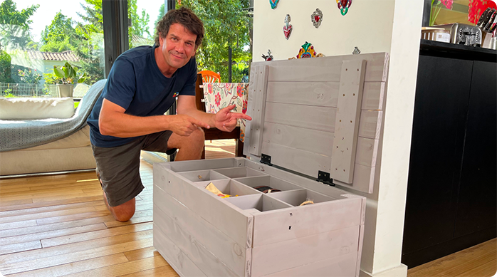 un hombre sonriente hincado al lado del baúl organizador que acaba de construir para ordenar sus hobbies.