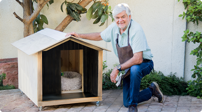 un hombre hincado muy feliz al lado de la casa para perro que acaba de construir.
