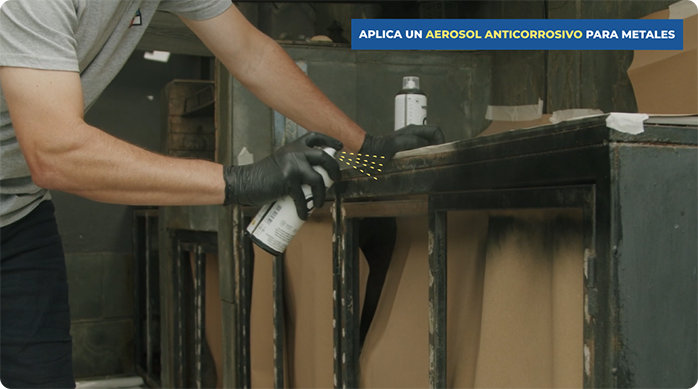 un hombre aplica pintura en spray en la estructura metálica de las puertas de un quincho.