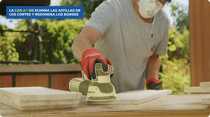 un hombre pasa una lijadora roto orbital para suavizar unas tablas de madera.