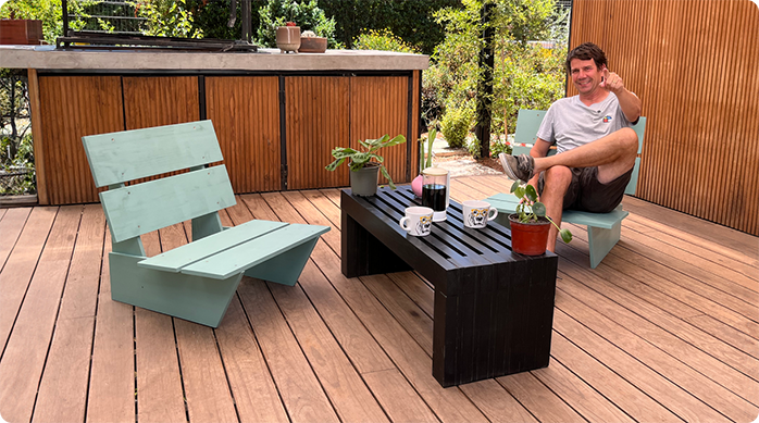 un hombre feliz sentado en un sofá de madera para terraza, junto a otro sofá idéntico y una mesa de centro.
