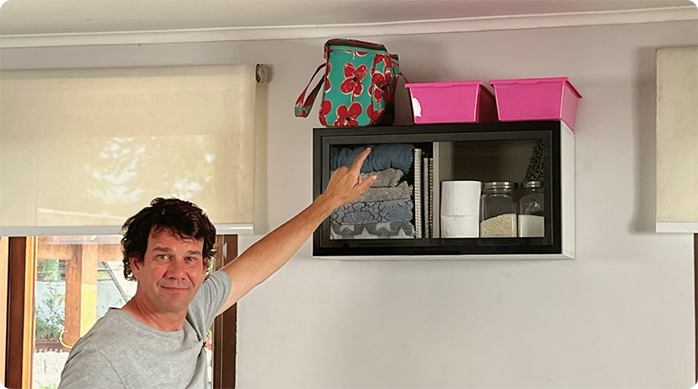 un hombre sonriendo indica con el dedo el mueble flotante que acaba de instalar en la pared para ahorrar espacio.