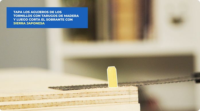 una persona corta el tarugo de madera que puso para tapar los agujeros de los tornillos usando una sierra japonesa.