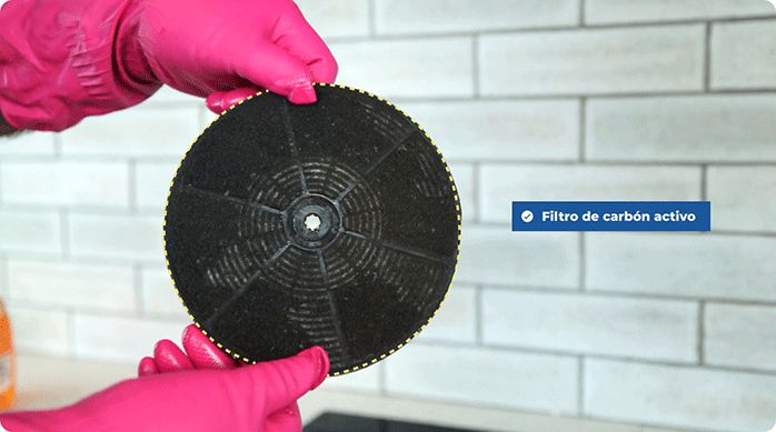 una persona sujeta un filtro de carbón activo de una campana de cocina.