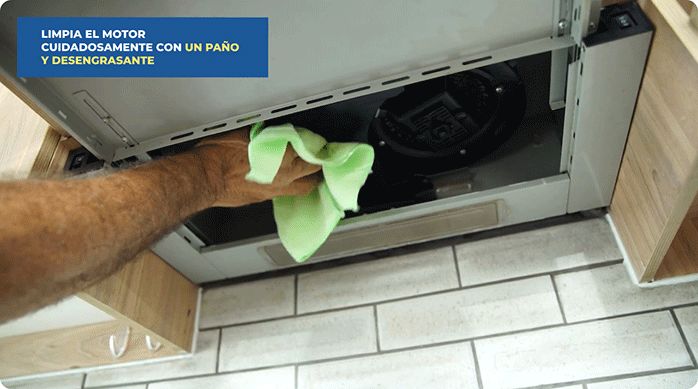 un hombre limpia el motor de una campana de cocina con un paño y desengrasante.