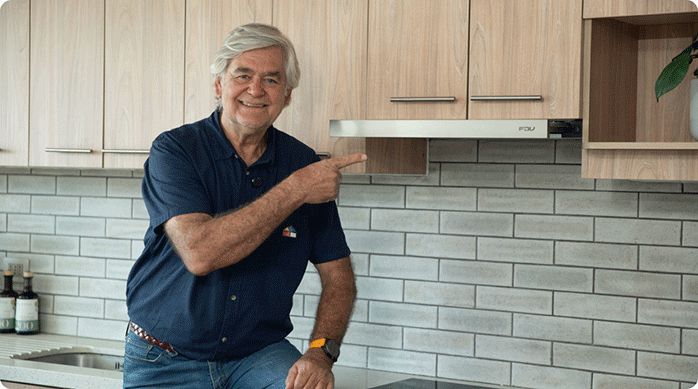 un hombre sonriente indica con el dedo la campana de cocina que acaba de limpiar.