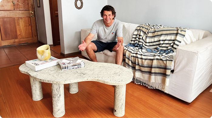 un hombre feliz sentado en un sillón en un living, frente a la mesa de centro estilo japandi que acaba de crear.