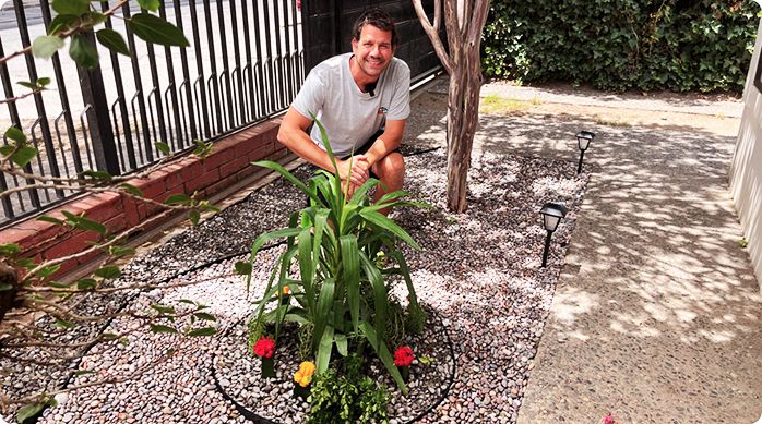 un hombre feliz hincado en el jardín de bajo mantenimiento con piedras y plantas que acaba de armar..