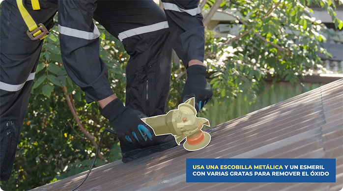 un hombre con overol y arnés usa un esmeril con grata en un techo de zinc para remover óxido y suciedad.