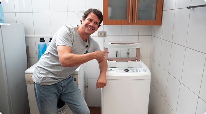 un hombre feliz apoyado en una lavadora apuntando con el dedo hacia ella.