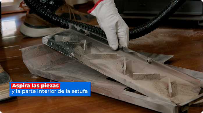 un hombre limpiando las partes móviles de una estufa a pellet con una aspiradora.