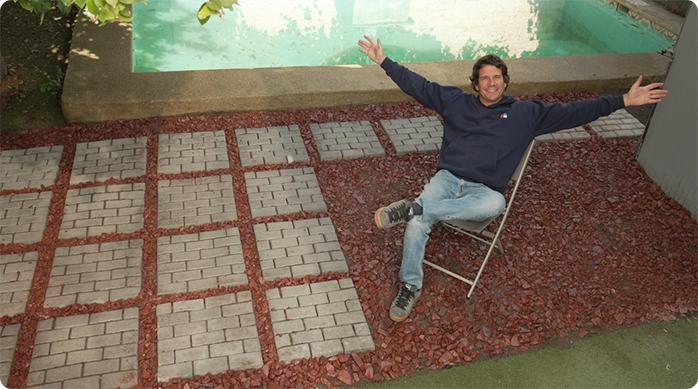 un hombre muy feliz sentado en una silla en un patio con un piso nuevo de adoquines modulares y gravilla.