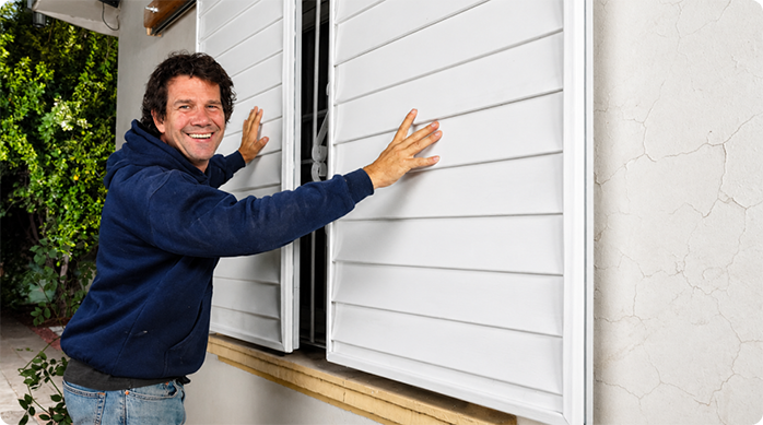 un hombre sonriendo frente a una ventana, en la que instaló protecciones correderas.