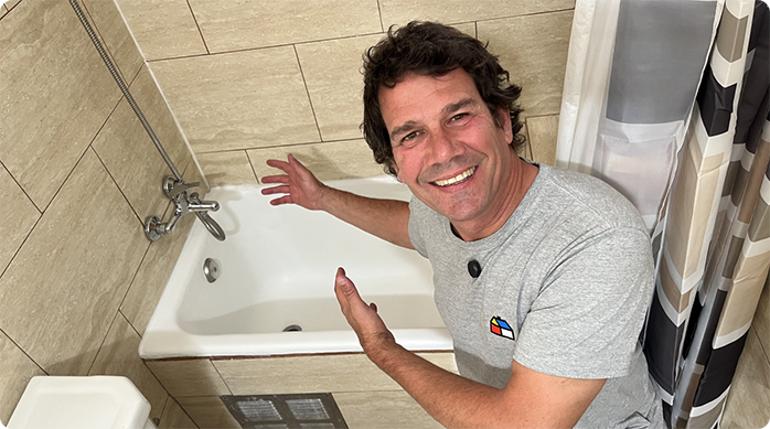 un hombre sonriendo y mostrando cómo quedó la tina de baño que acaba de renovar.