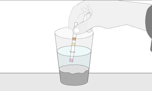 vaso con agua y tierra y una mano sosteniendo dentro de este un medidor de PH